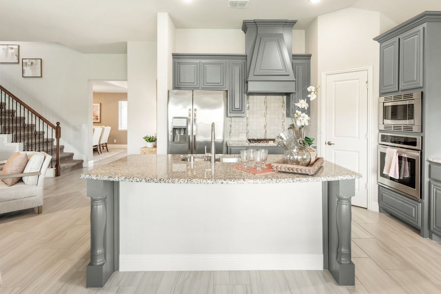 Kitchen with large granite island, gray cabinets, stainless steel appliances, and decorative range hood