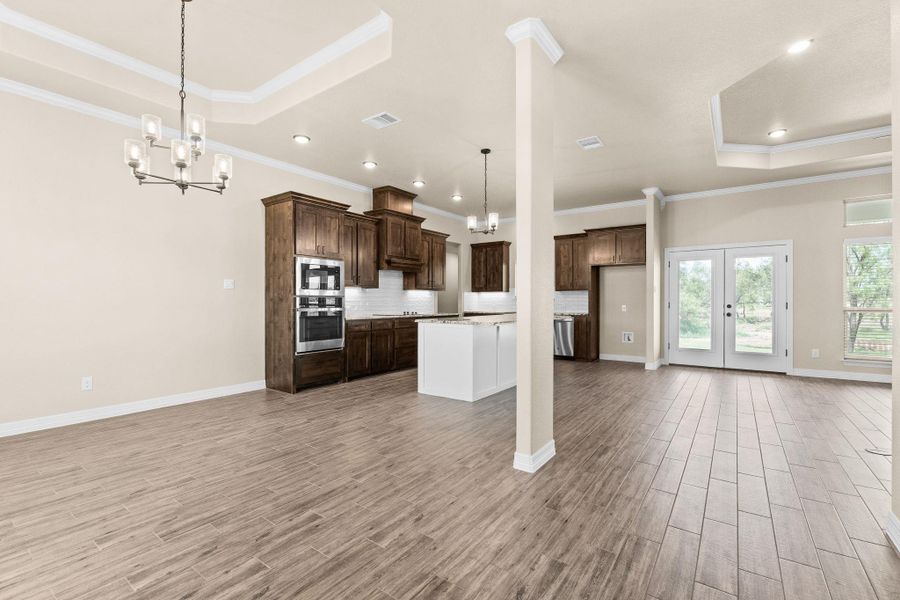 Kitchen featuring a tray ceiling, a chandelier, open floor plan, crown molding, and pendant lighting Kitchen featuring a tray ceiling, a chandelier, open floor plan, crown molding, and pendant lighting