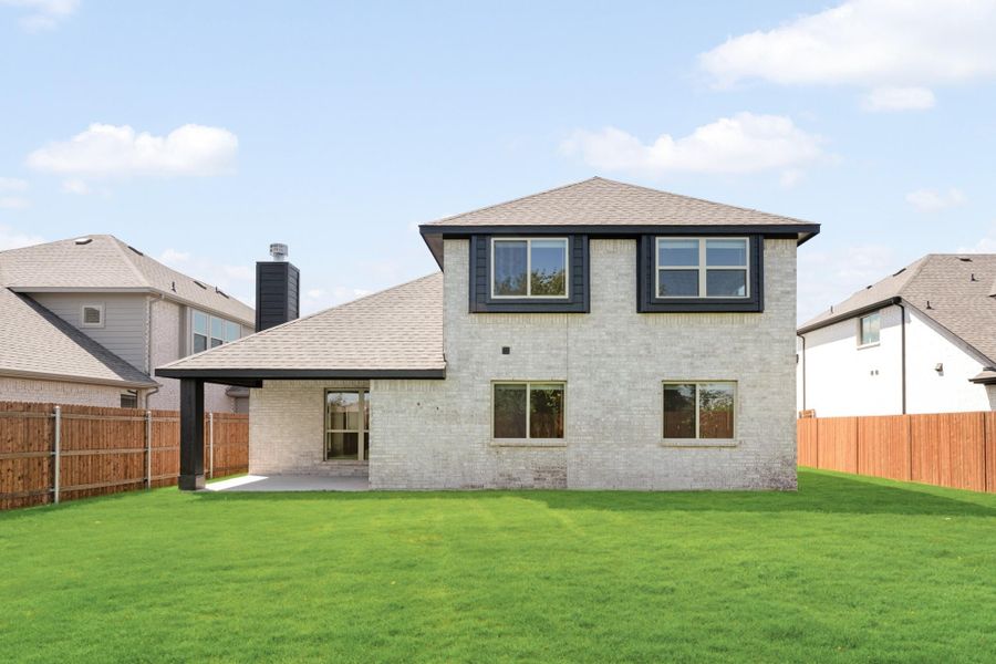 Two-story home with light brick exterior, covered patio, and fenced backyard with green lawn