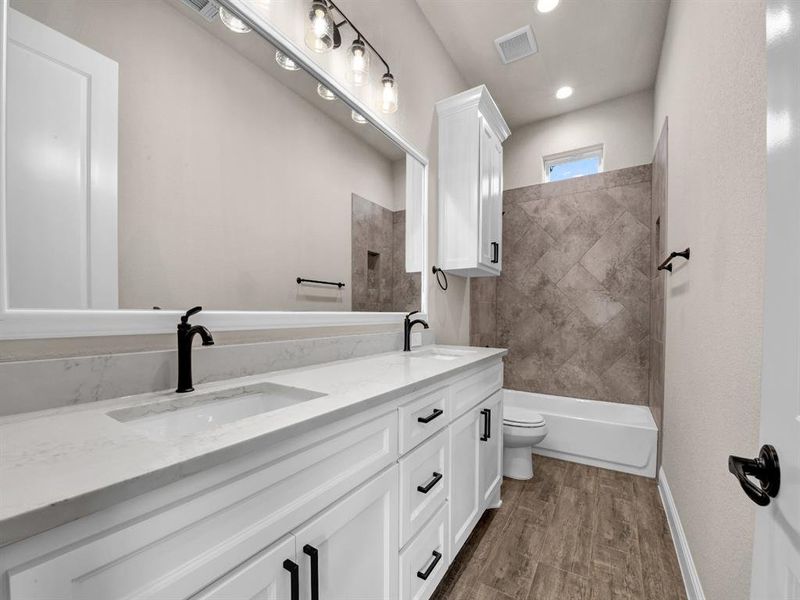 Full bathroom with wood-type flooring, dual vanity, toilet, and tiled shower / bath