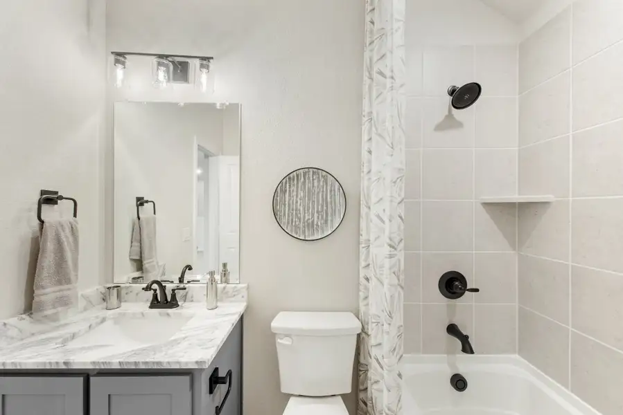 Bathroom with marble countertop vanity, white tile tub-shower combo, and black fixtures