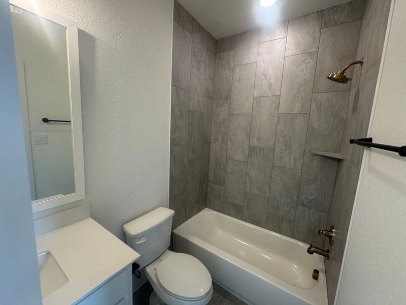 Bathroom featuring a white vanity with an integrated sink and white countertop, a toilet, and a shower-over-tub combination