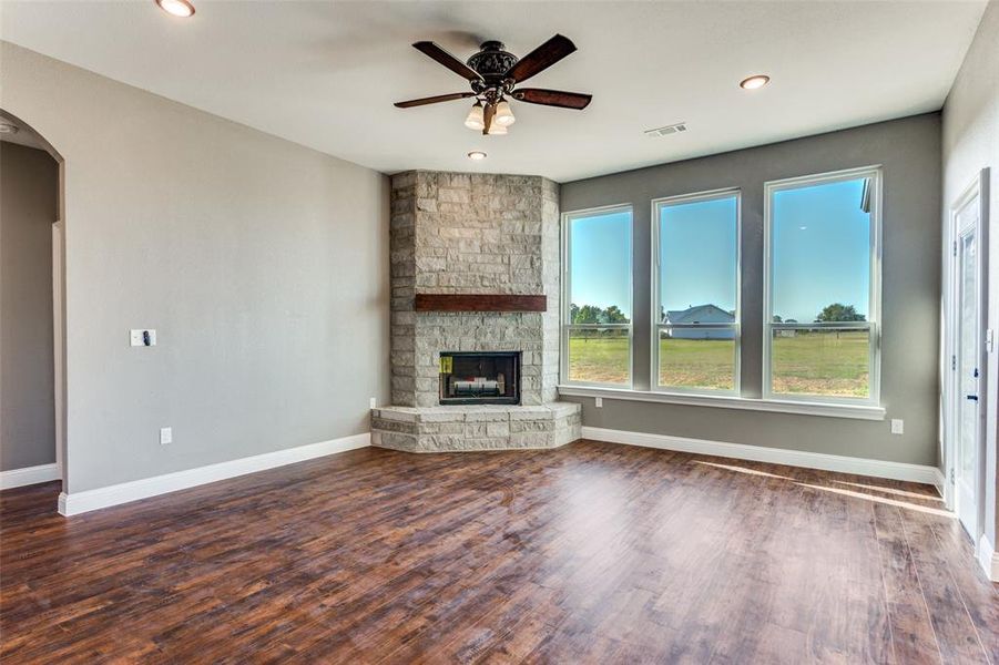 Unfurnished living room with arched walkways, dark wood-style floors, a stone fireplace, ceiling fan, and recessed lighting Unfurnished living room with arched walkways, dark wood-style floors, a stone fireplace, ceiling fan, and recessed lighting