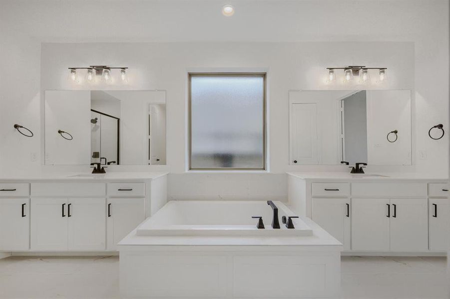 Bathroom featuring a built-in tub, dual vanities with white cabinetry, quartz countertops, and matte black fixtures