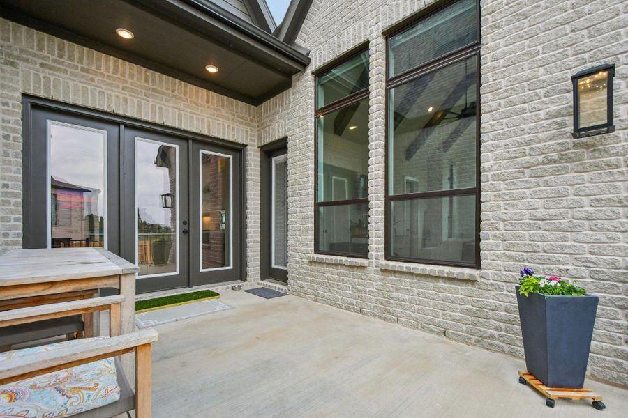 The property features a light-colored brick exterior with large windows and a pair of glass-paneled doors, complemented by exterior lighting fixtures The property features a light-colored brick exterior with large windows and a pair of glass-paneled doors, complemented by exterior lighting fixtures