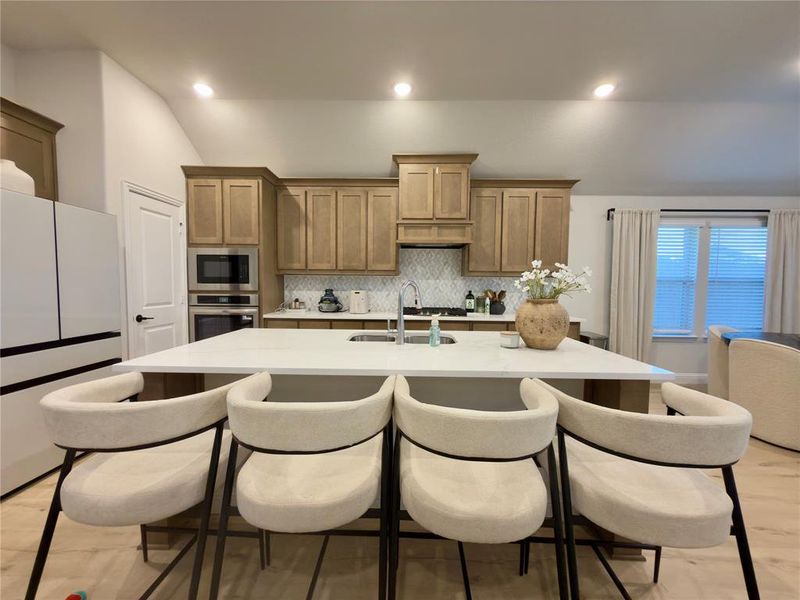 Kitchen featuring a kitchen breakfast bar, vaulted ceiling, stainless steel appliances, a center island with sink, and tasteful backsplash
