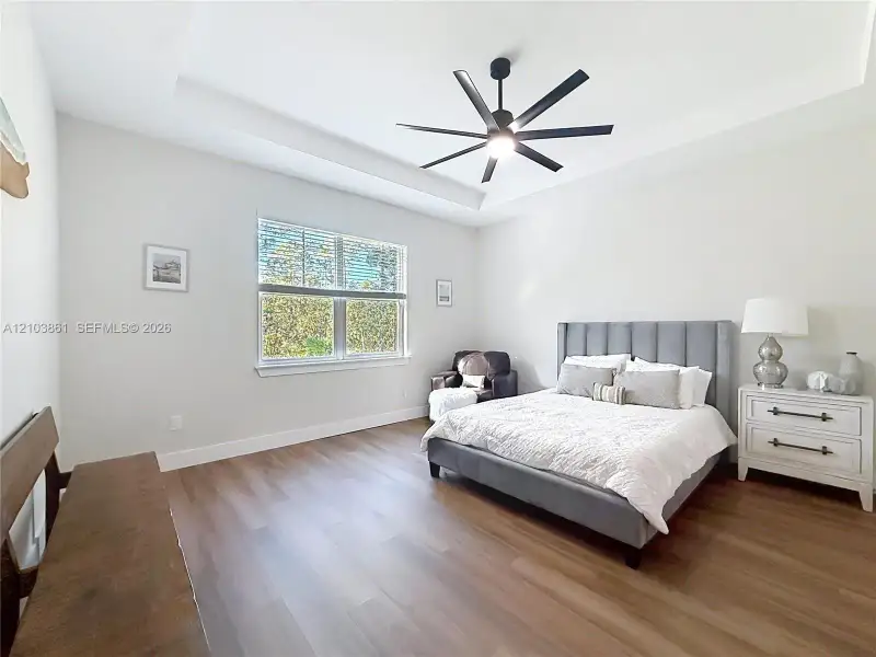 Tray ceiling with integrated lighting, wood-finish flooring, and a multi-blade ceiling fan