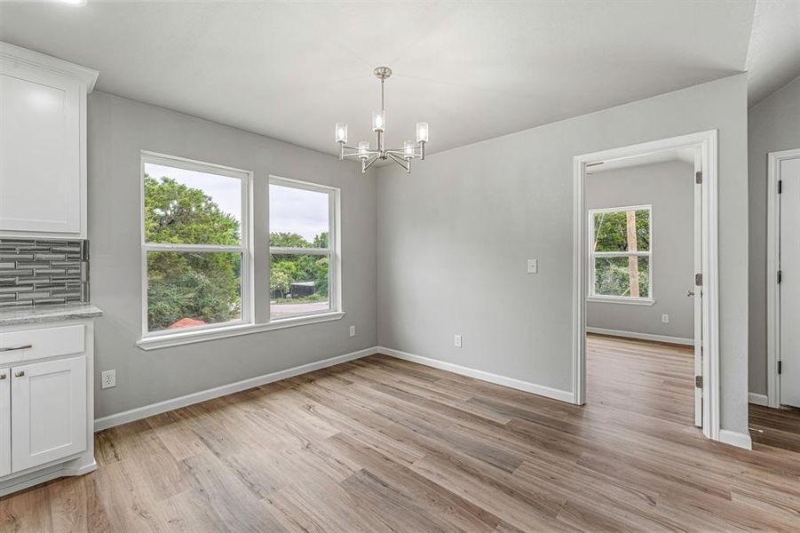 Unfurnished dining area with a chandelier, light wood-style flooring, and baseboards Unfurnished dining area with a chandelier, light wood-style flooring, and baseboards