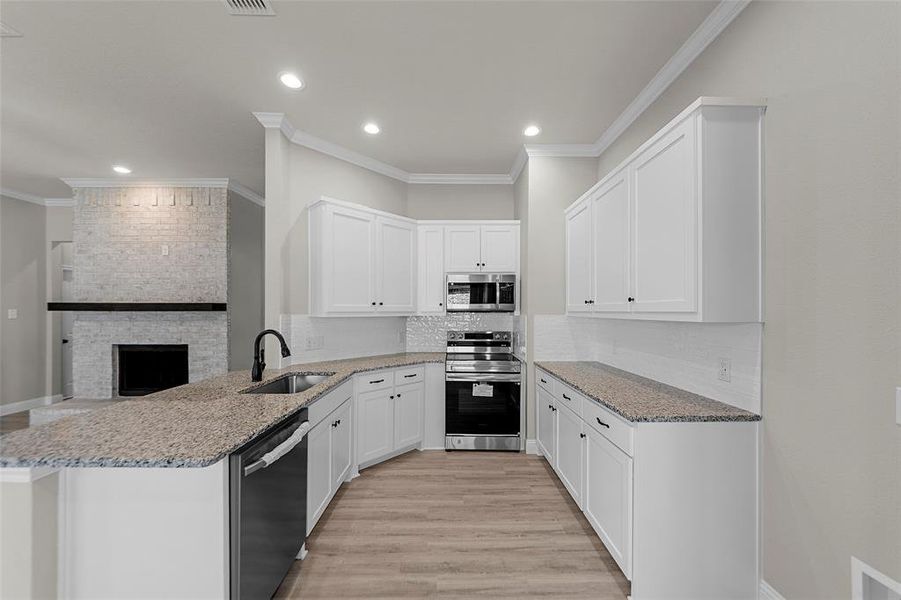 Kitchen featuring stainless steel appliances, a peninsula, white cabinets, light stone counters, and ornamental molding