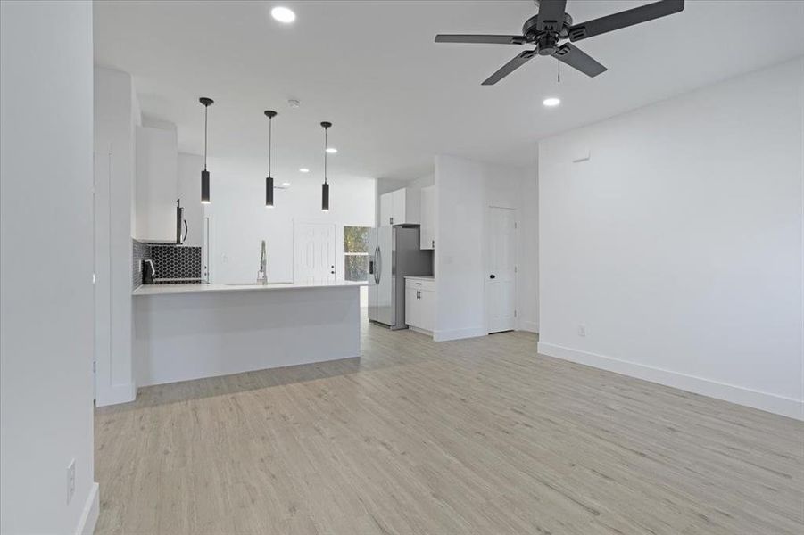 Unfurnished living room featuring light wood-type flooring, ceiling fan, and sink