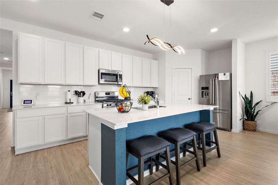 Modern kitchen with sleek white cabinets, stainless steel appliances, and a spacious island with seating. The light wood flooring and contemporary lighting fixture add warmth and style.