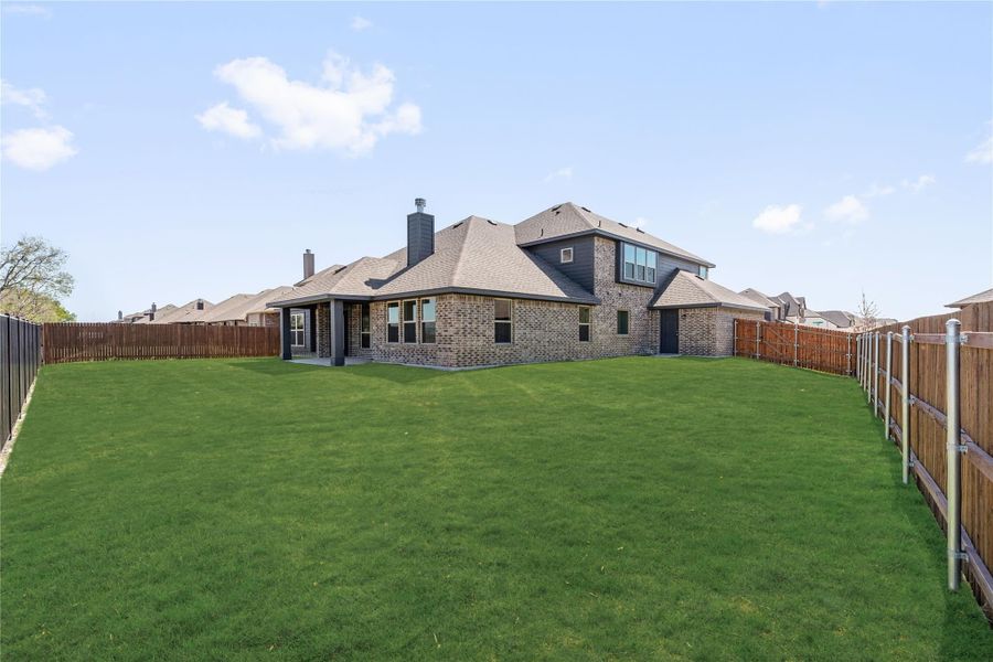 Rear view of two-story brick home with large grassy backyard and wood privacy fence