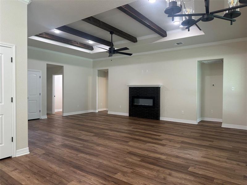 Unfurnished living room with a ceiling fan, beam ceiling, dark wood finished floors, crown molding, and a glass covered fireplace Unfurnished living room with a ceiling fan, beam ceiling, dark wood finished floors, crown molding, and a glass covered fireplace