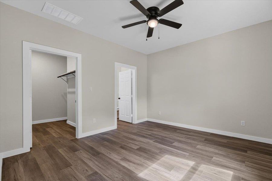 A spacious bedroom features neutral walls and wood-look flooring. A spacious bedroom features neutral walls and wood-look flooring.