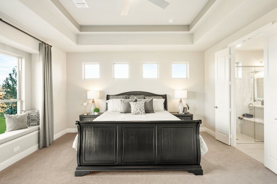 Master bedroom with tray ceiling, dark wood sleigh bed, window seat, and ensuite bathroom visible through open door Master bedroom with tray ceiling, dark wood sleigh bed, window seat, and ensuite bathroom visible through open door
