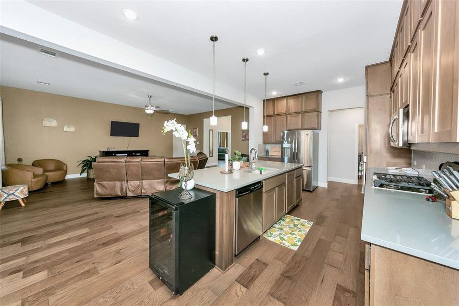 Kitchen with sink, stainless steel appliances, decorative light fixtures, light hardwood / wood-style flooring, and a center island with sink