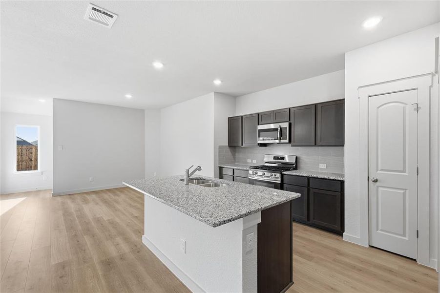 Kitchen featuring stainless steel appliances, a center island with sink, light stone countertops, recessed lighting, and light wood-style flooring