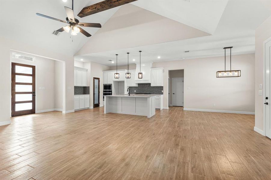 Kitchen with backsplash, open floor plan, white cabinets, a kitchen island with sink, and light wood finished floors