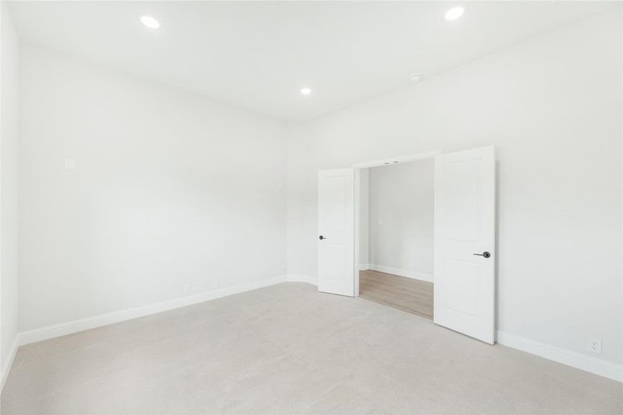 Empty bedroom with beige carpet, white walls, recessed lighting, and two doors leading to a closet or hallway.