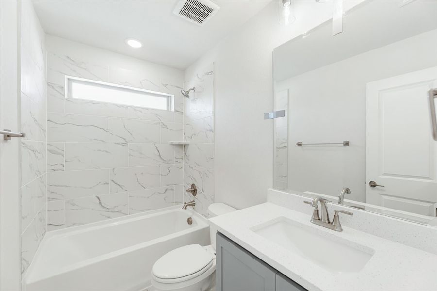 Bathroom with marble-look tile tub surround, white quartz vanity, and large mirror