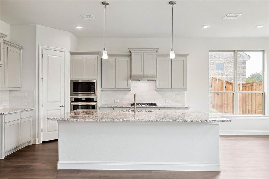 Kitchen with wood-type flooring, gray cabinets, stainless steel appliances, and backsplash