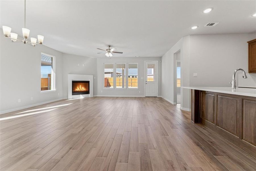 Unfurnished living room with a lit fireplace, light wood-type flooring, recessed lighting, and ceiling fan