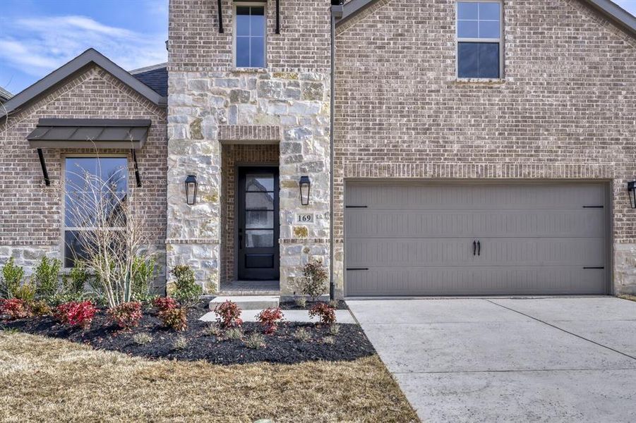 View of front of house featuring concrete driveway, brick siding, an attached garage, and stone siding