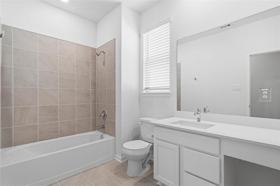 Well-appointed secondary bath with tub/shower combination and tile surround. It also features an extended vanity with a light countertop, a mirror that extends the full length of the vanity, and a window with blinds allowing in the natural light!