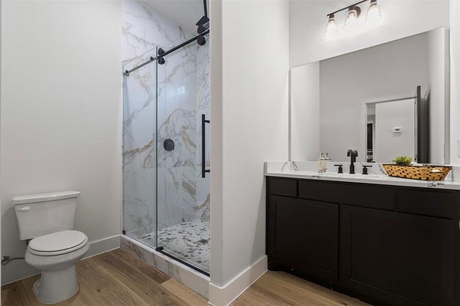 Bathroom with a marble finish shower, light wood-style floors, and vanity