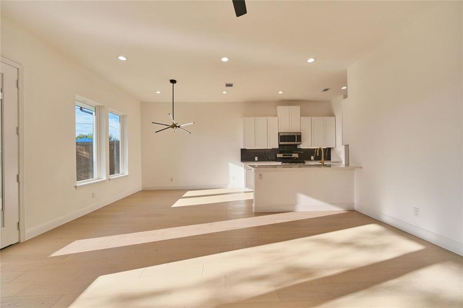 Kitchen with tasteful backsplash, white cabinets, kitchen peninsula, stainless steel appliances, and decorative light fixtures