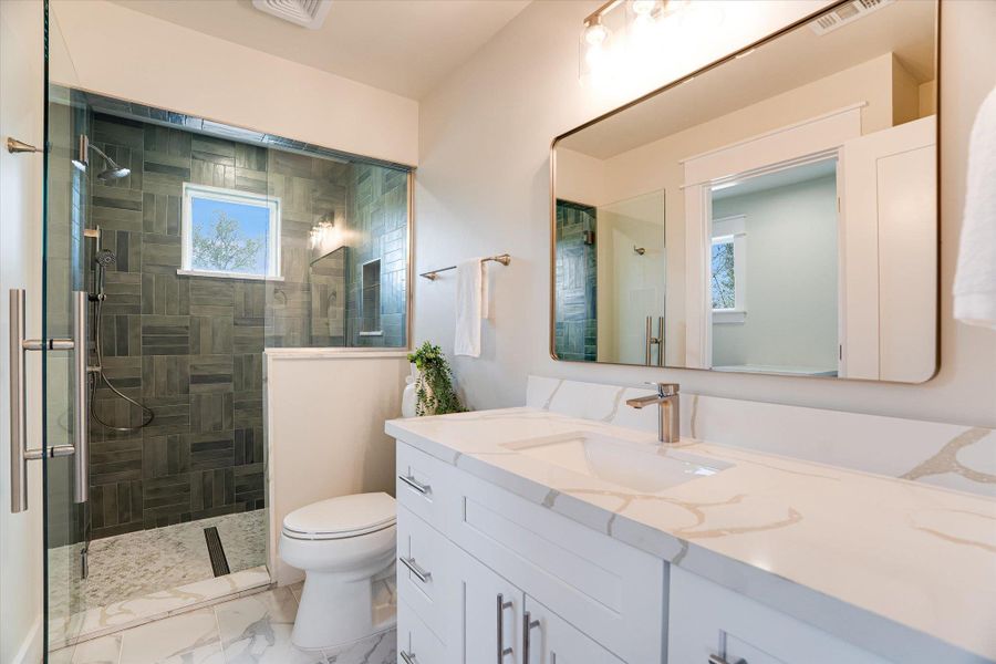 Contemporary bathroom featuring a spacious shower with dark tiled walls, a window for natural light, and a white vanity with a light-colored countertop Contemporary bathroom featuring a spacious shower with dark tiled walls, a window for natural light, and a white vanity with a light-colored countertop
