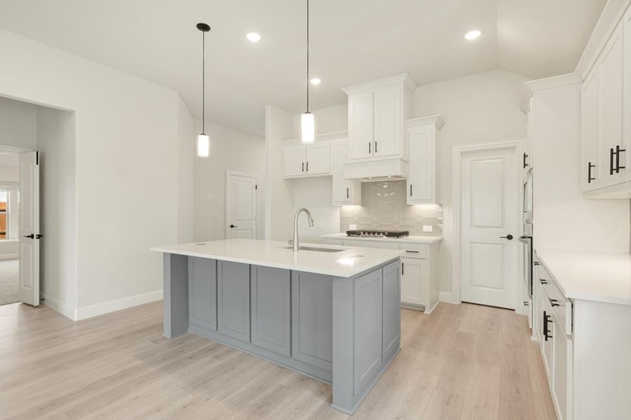 Kitchen with white cabinets, gray island with sink, pendant lights, and light wood floors