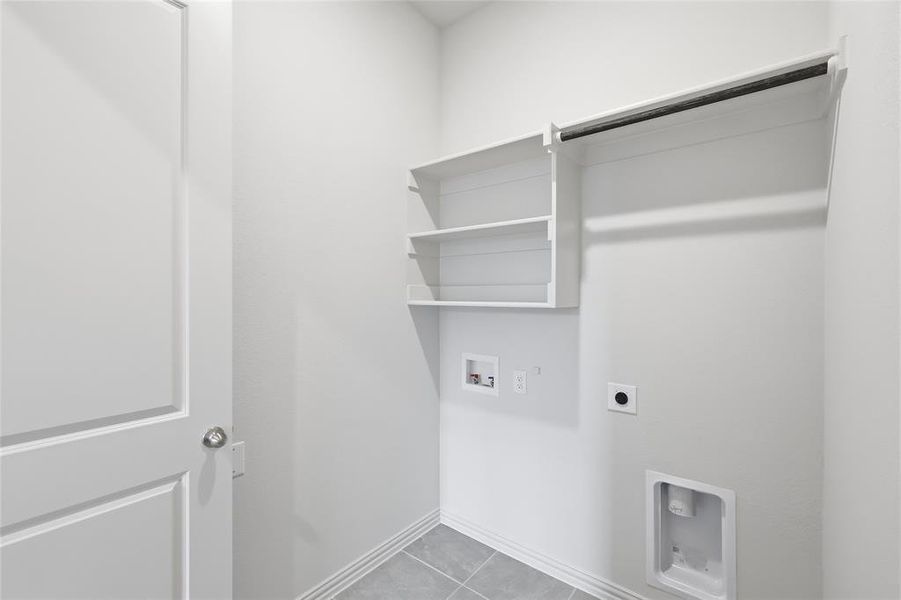 Laundry area featuring an overhead clothes hanging rod, built-in shelving, and light gray tile flooring Laundry area featuring an overhead clothes hanging rod, built-in shelving, and light gray tile flooring