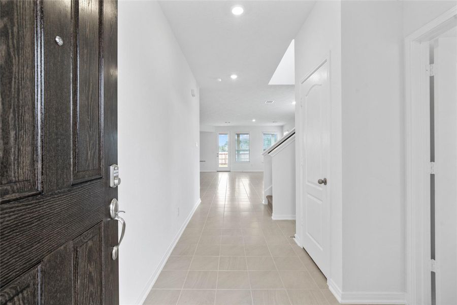 Upon entering this gorgeous home, a lovely corridor features custom paint, beautiful Coastline ceramic tile floors, high ceilings, recessed lighting and a coat closet!