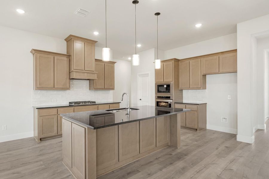 Kitchen with tan wood cabinets, dark granite island, pendant lights, and hardwood floors