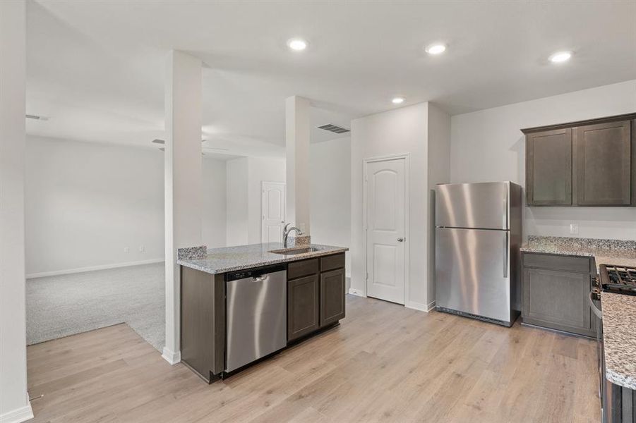 Kitchen with appliances with stainless steel finishes, light stone counters, dark brown cabinetry, light wood-style floors, and recessed lighting
