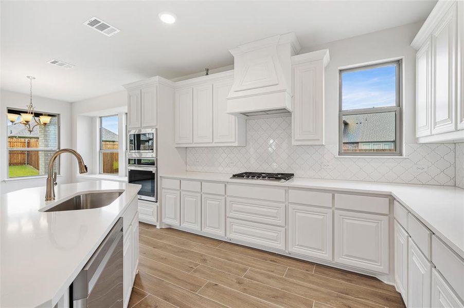 Kitchen with wood finish floors, decorative backsplash, appliances with stainless steel finishes, white cabinetry, and decorative light fixtures