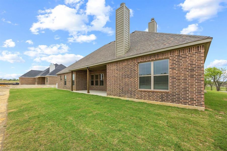 Brick exterior featuring a covered patio, multiple windows, and a shingled roof
