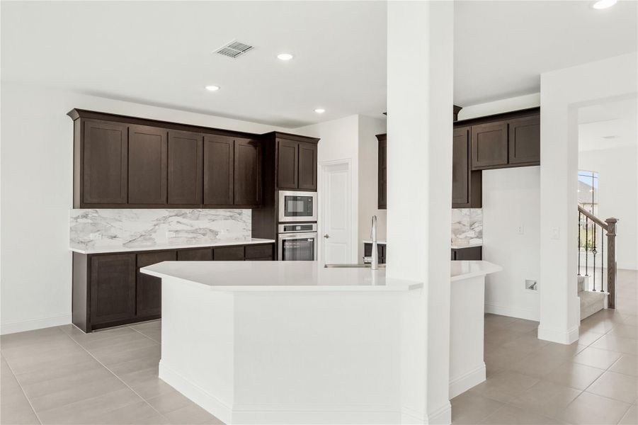 Kitchen with dark brown cabinets, marble backsplash, white island, and stainless steel appliances on tile floors Kitchen with dark brown cabinets, marble backsplash, white island, and stainless steel appliances on tile floors