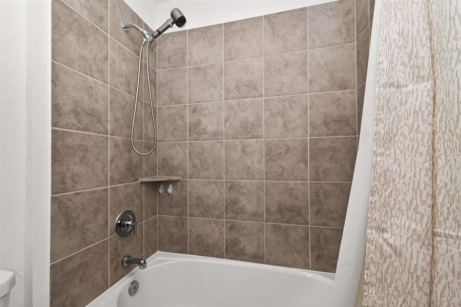 Upstairs bathroom featuring a tub/shower combination with tile surround, neutral finishes, and built-in corner shelving for added storage and convenience. Clean layout designed to serve secondary bedrooms and guest spaces.