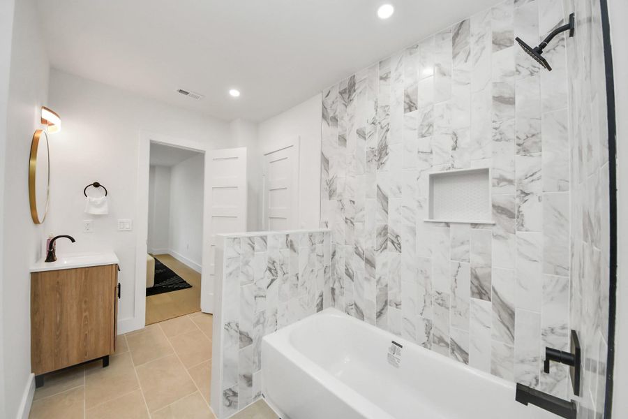 This modern shared bathroom features a sleek design with a marble-tiled shower and bathtub, a stylish wooden vanity with a round mirror, and neutral tile flooring. This modern shared bathroom features a sleek design with a marble-tiled shower and bathtub, a stylish wooden vanity with a round mirror, and neutral tile flooring.