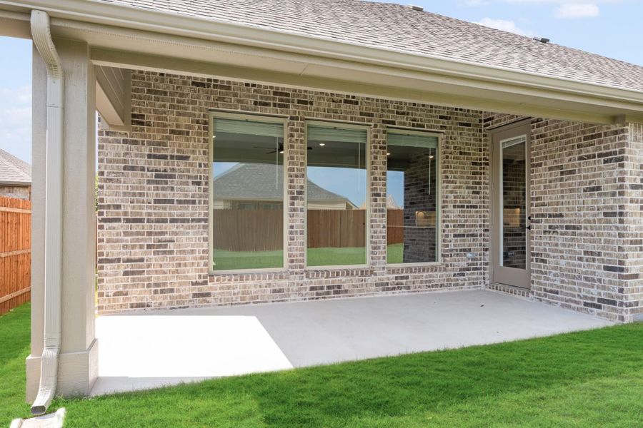 Covered back patio with concrete slab, brick exterior, large windows, and green lawn