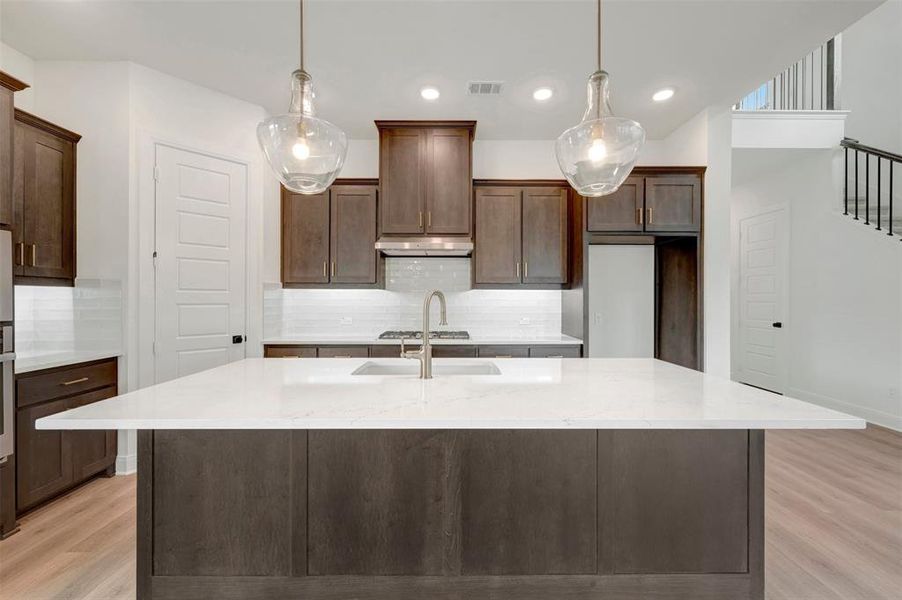 Kitchen featuring a large island with a light-toned countertop, dark wood cabinetry, and pendant lighting