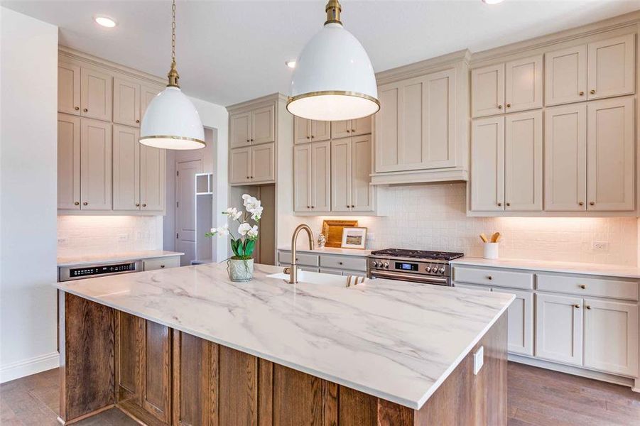 Kitchen with tasteful backsplash, dark wood-style floors, hanging light fixtures, light stone counters, and stainless steel gas range Kitchen with tasteful backsplash, dark wood-style floors, hanging light fixtures, light stone counters, and stainless steel gas range