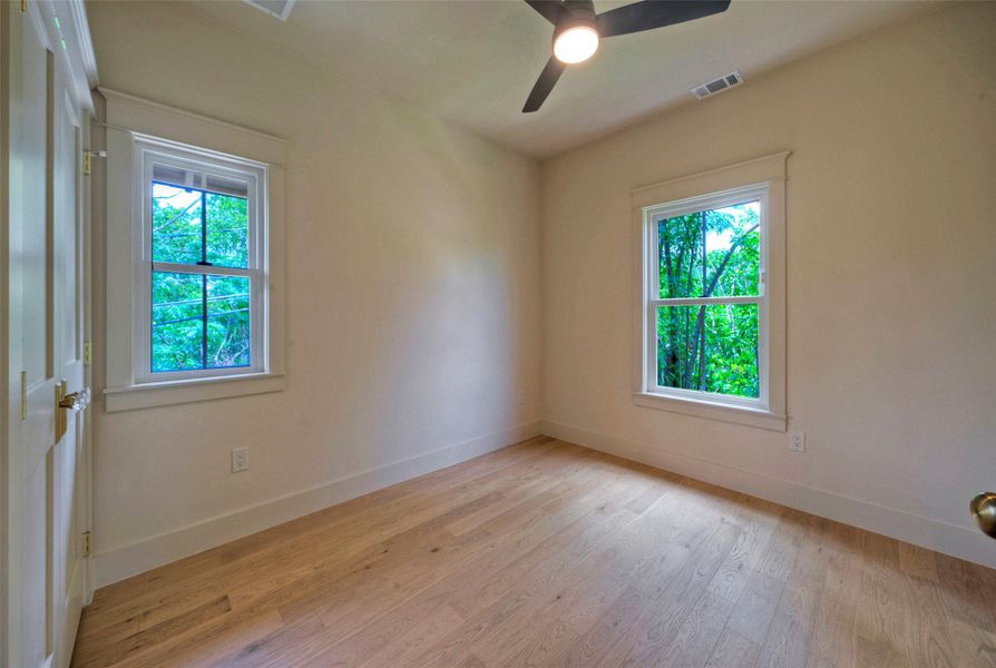 Sun-filled Bedroom #2 featuring light wood flooring and a refreshing tree-lined view from two windows.