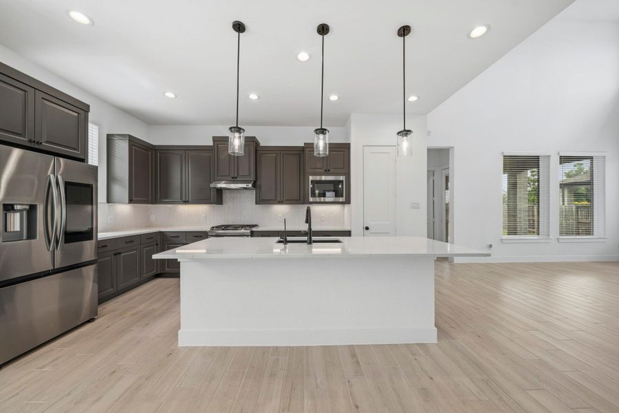 The kitchen boasts a large island with a sleek black faucet and large single basin sink. Finished with built-in stainless steel appliances, pendant lighting, and black cabinet hardware, this kitchen is ideal for cooking for the whole family or hosting holidays!