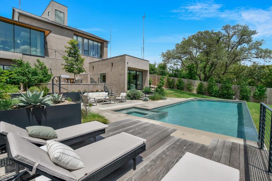 Contemporary stucco exterior with expansive window walls, multi-level terraces, a rectangular swimming pool with integrated spa, and a wood-finish deck