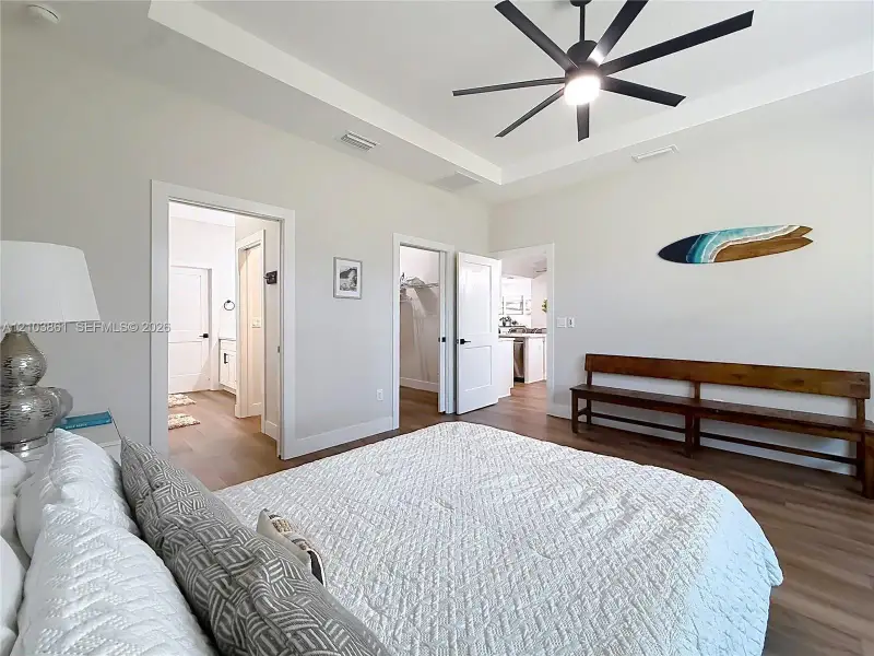 Tray ceiling featuring a multi-blade matte black ceiling fan, complemented by wood-finish flooring and solid-core interior doors