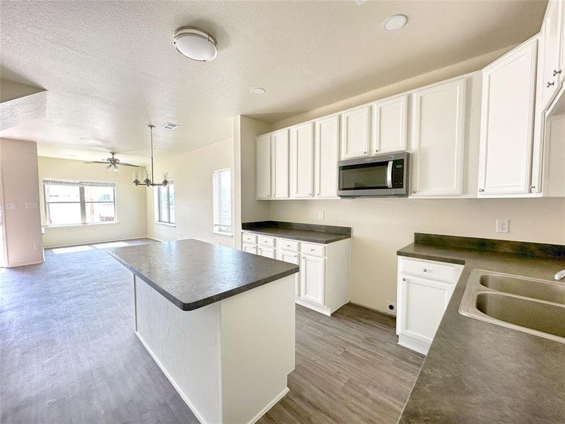 Kitchen featuring dark countertops, stainless steel microwave, white cabinetry, a kitchen island, and open floor plan