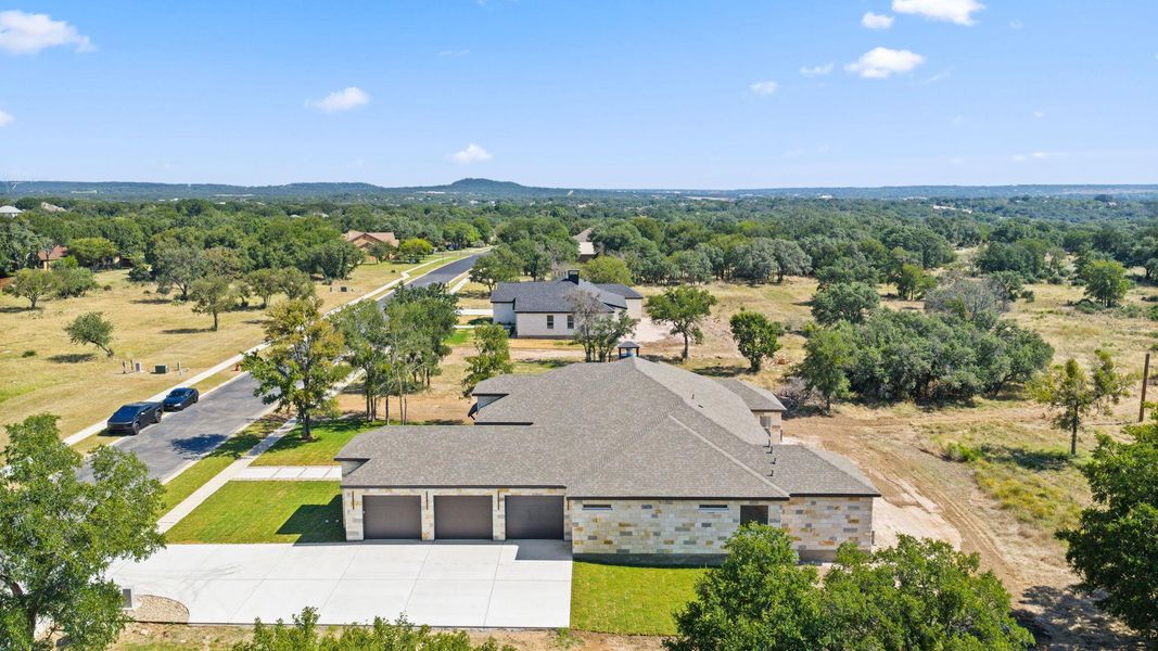 An aerial perspective showcases a sprawling residence with a three-car garage and a broad concrete driveway amidst a lush, tree-dotted landscape. An aerial perspective showcases a sprawling residence with a three-car garage and a broad concrete driveway amidst a lush, tree-dotted landscape.